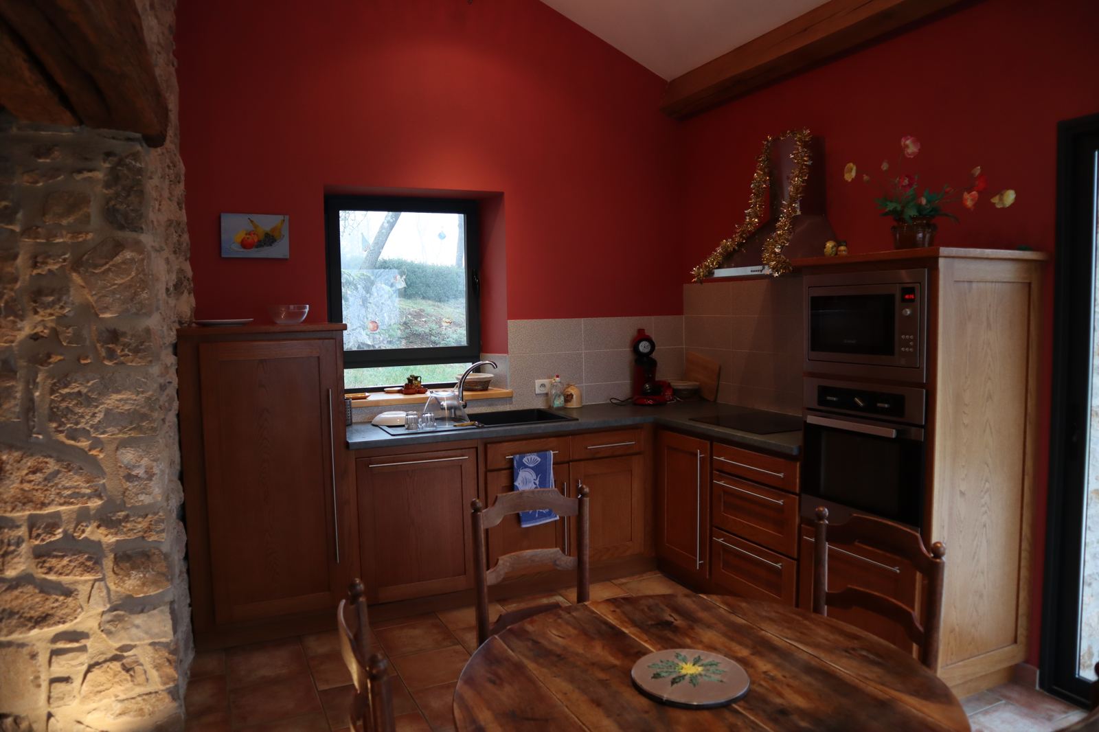 Fitted kitchen at Le Rouge Gorge gîte, red wall and exposed stone